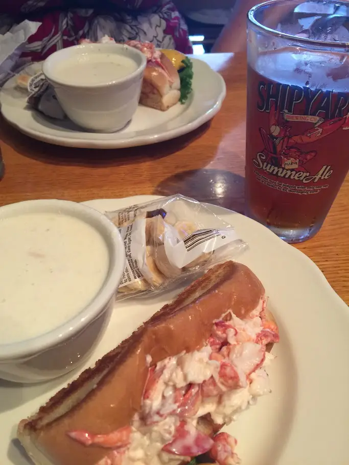 A lobster roll on a griddled bun with a cup of clam chowder and a glass of Shipyard summer ale