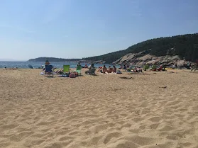 Beachgoers in green chairs on the sand at Sand Beach in Acadia with a granite headland behind