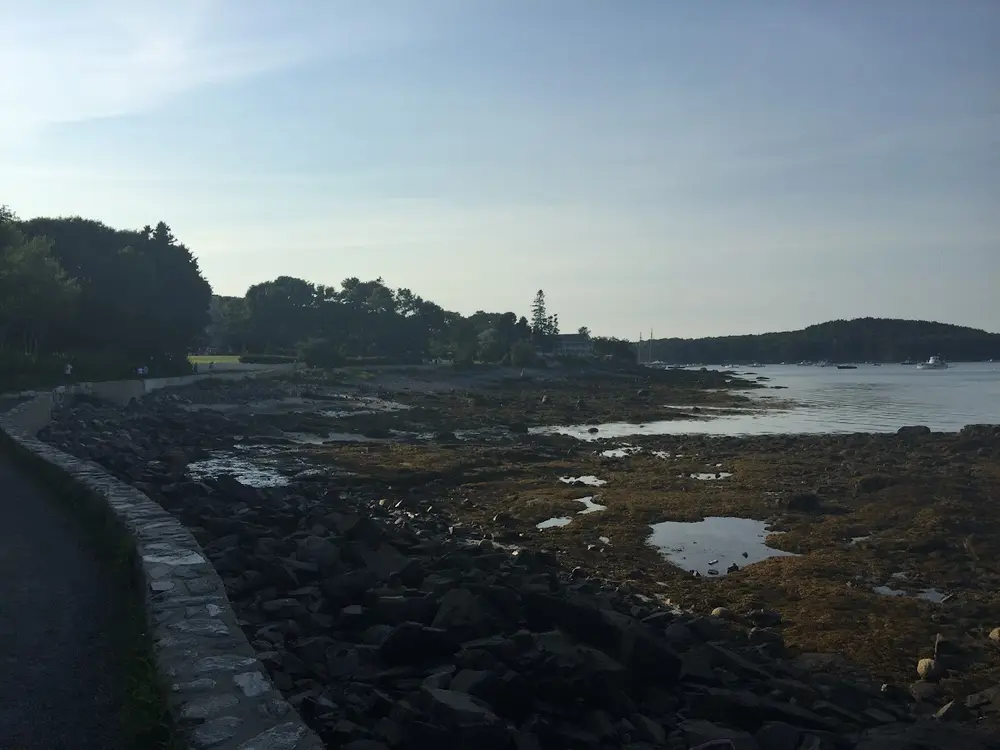 The stone lined Shore Path along Bar Harbor at low tide with the harbor islands in the distance