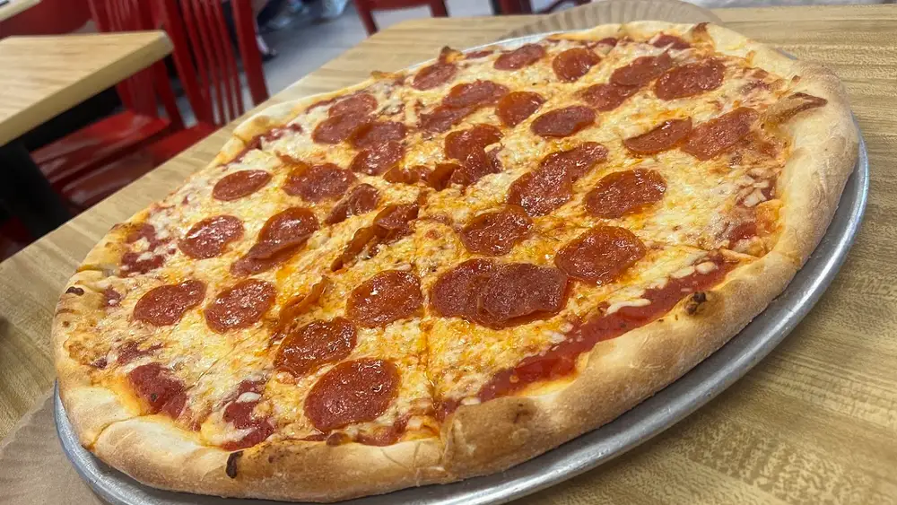A large thin-crust pepperoni pizza on a metal tray at Mario's in Cape May, red chairs behind it