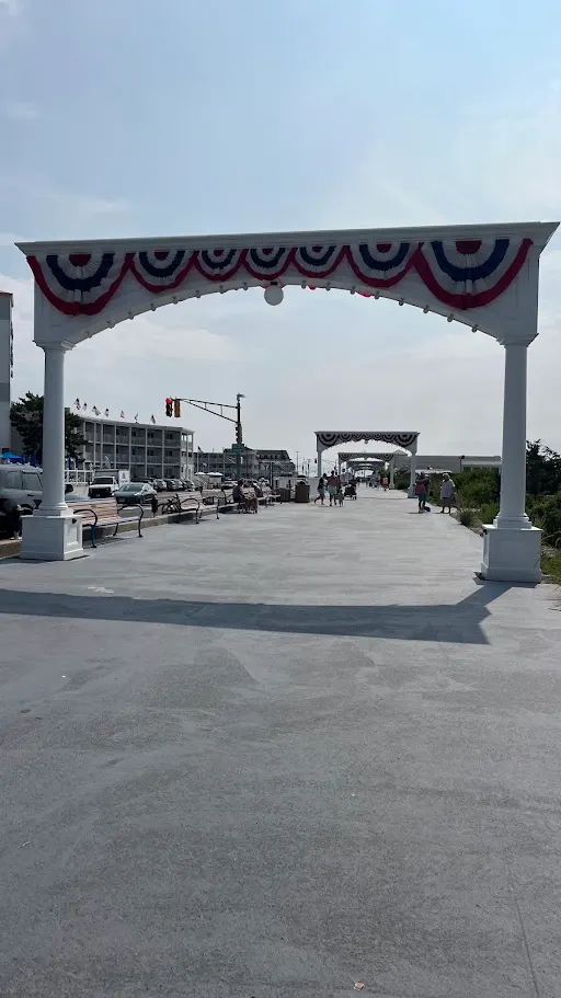 A white bunting-draped arch marking the entrance to the paved Cape May Promenade, Convention Hall in the distance