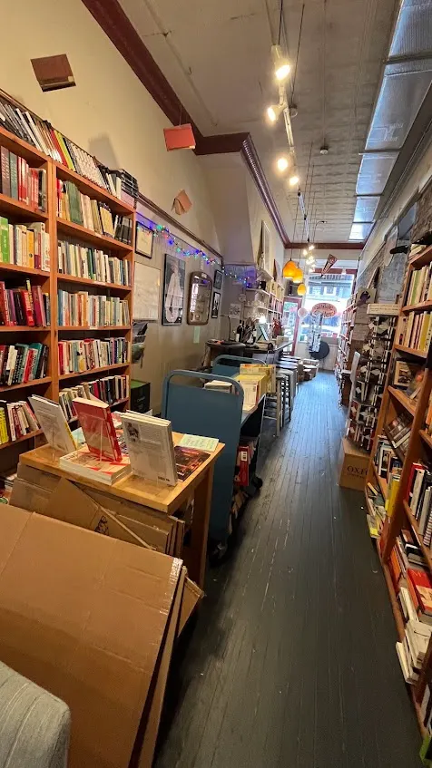The narrow interior of the Bookstore in Lenox, tall wooden shelves down both sides of a wood-floored aisle leading to the front window