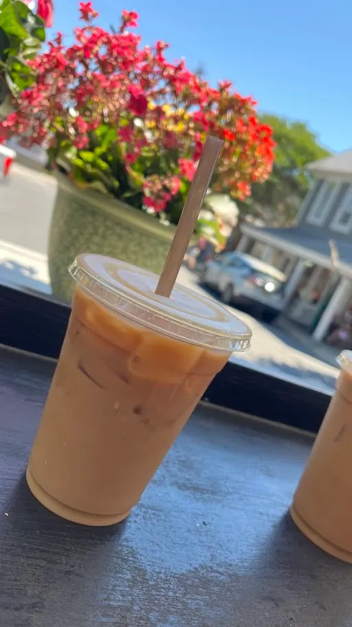 An iced coffee on a windowsill with a pot of red geraniums and a Lewes side street in the background