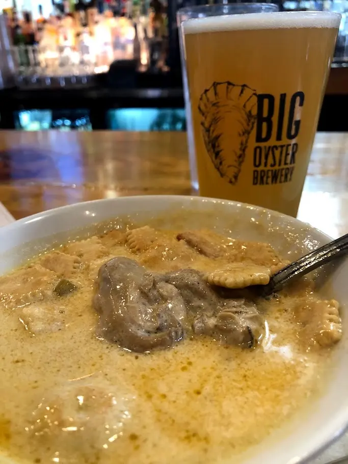 A bowl of creamy oyster soup with oyster crackers and a hazy beer at the bar of Big Oyster Brewery in Lewes