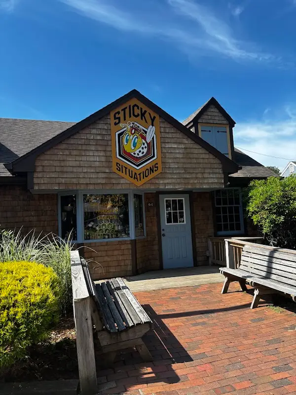 The shingled storefront of Sticky Situations in Olde Mistick Village, with wooden benches and a brick courtyard out front