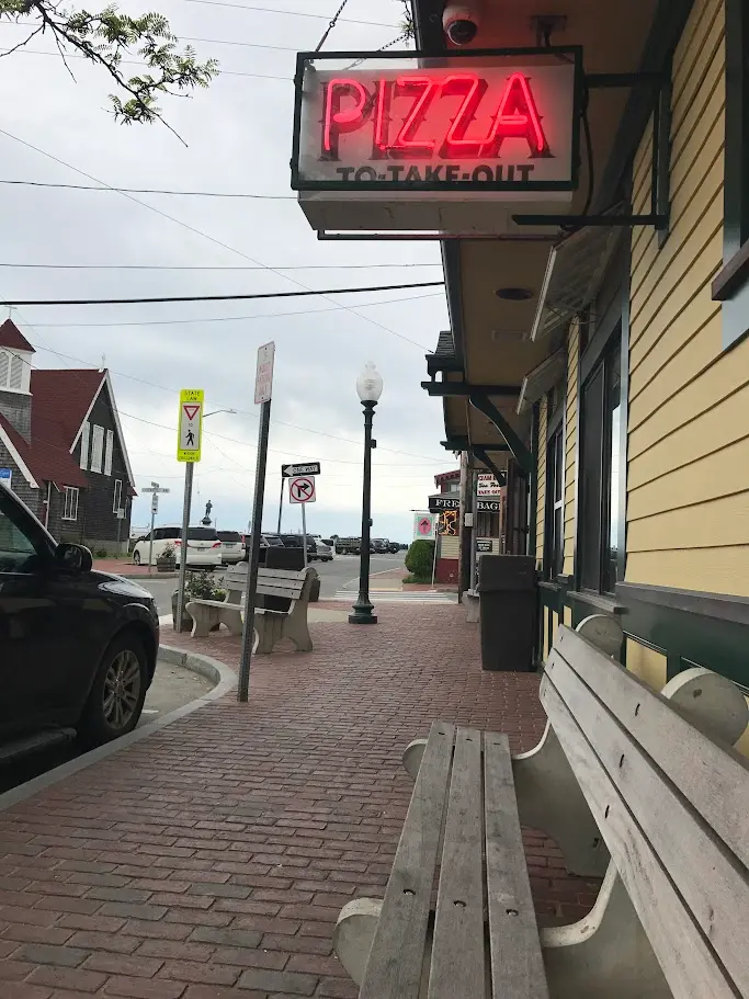 The red neon PIZZA TO TAKE OUT sign hanging over the sidewalk outside Giordano's in Oak Bluffs